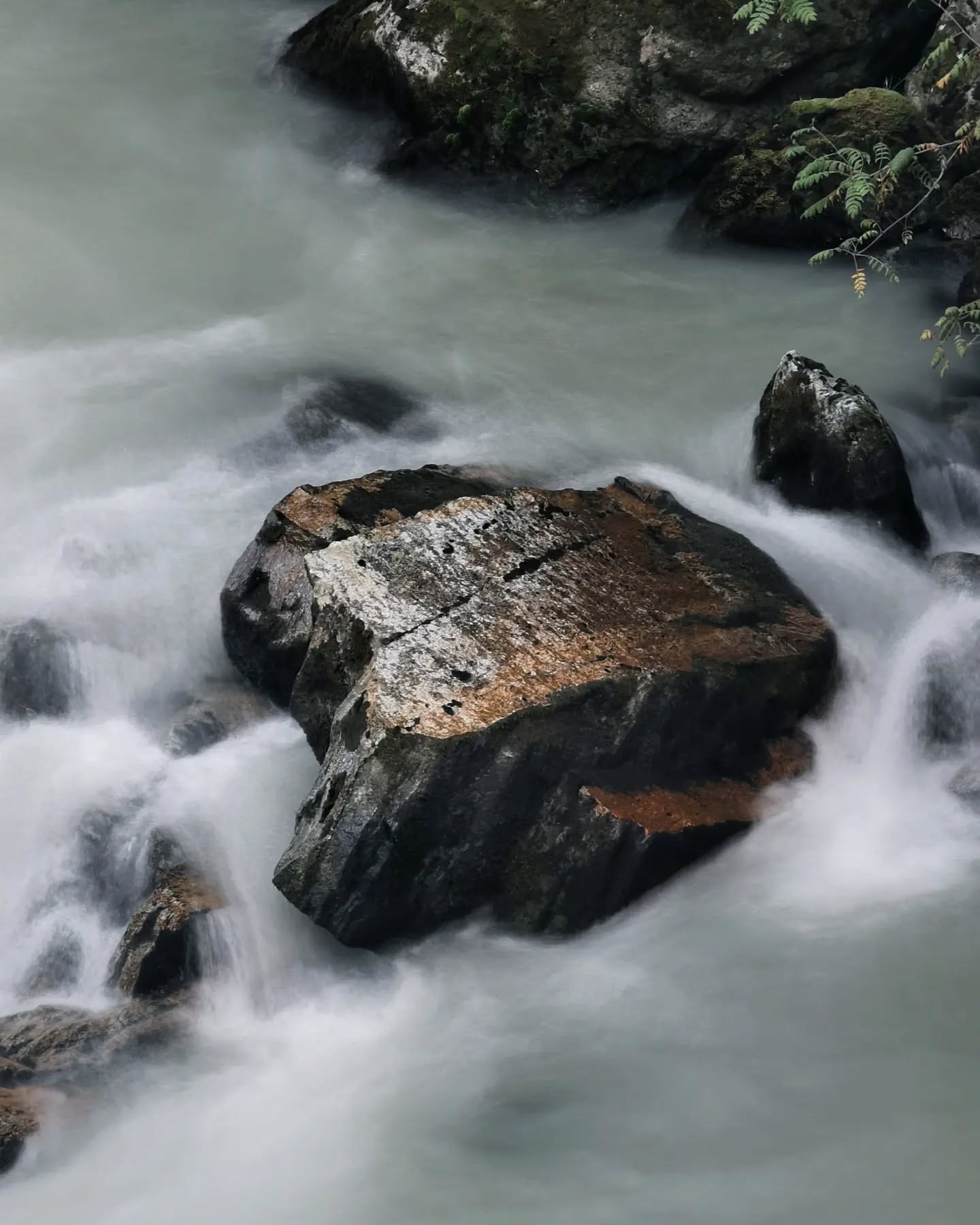 A long exposure of river water sliding past a lichen-covered boulder