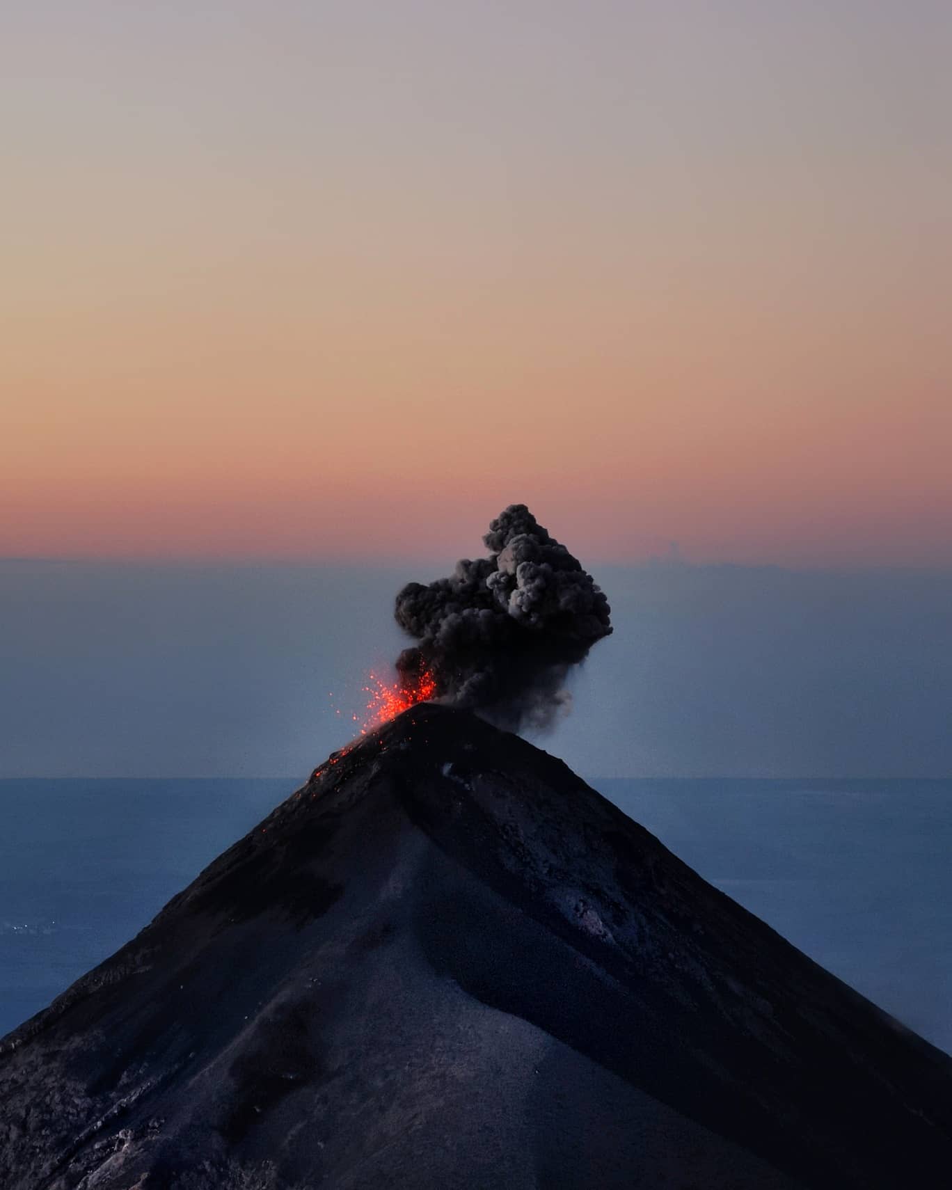 A volcano erupting at dusk, lava glowing at the vent
