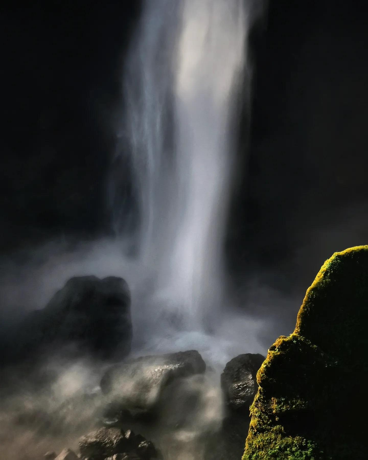 A waterfall landing among wet boulders and moss