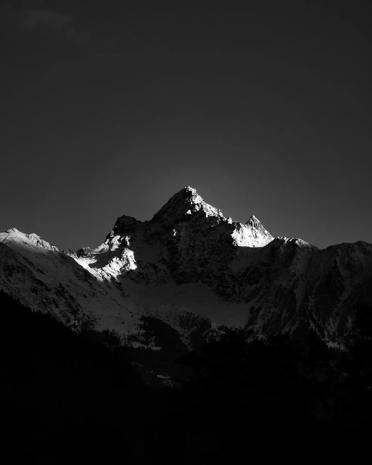 A dark jagged peak against a pale sky, in black and white