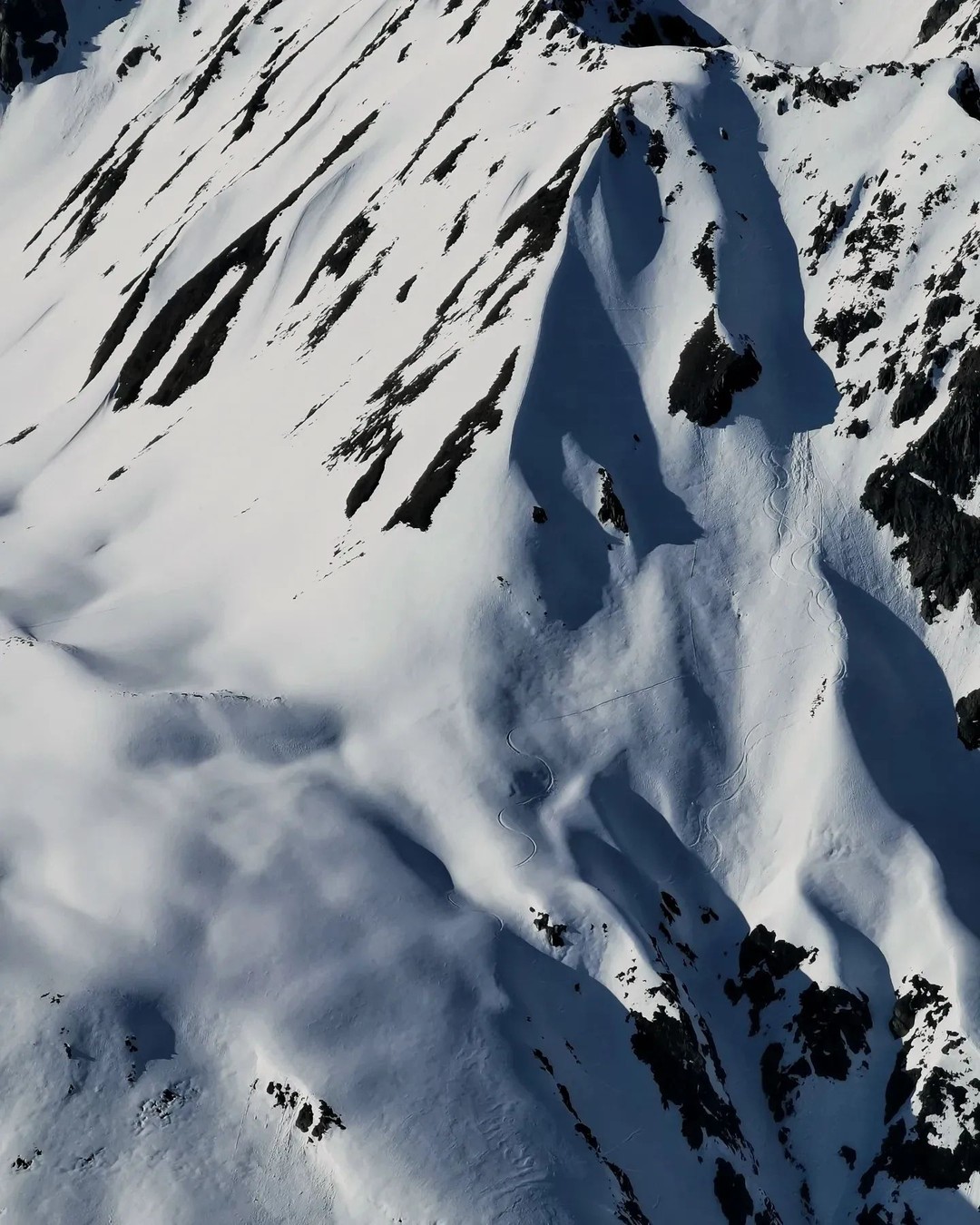 Snow-covered slopes and dark rock outcrops seen from above