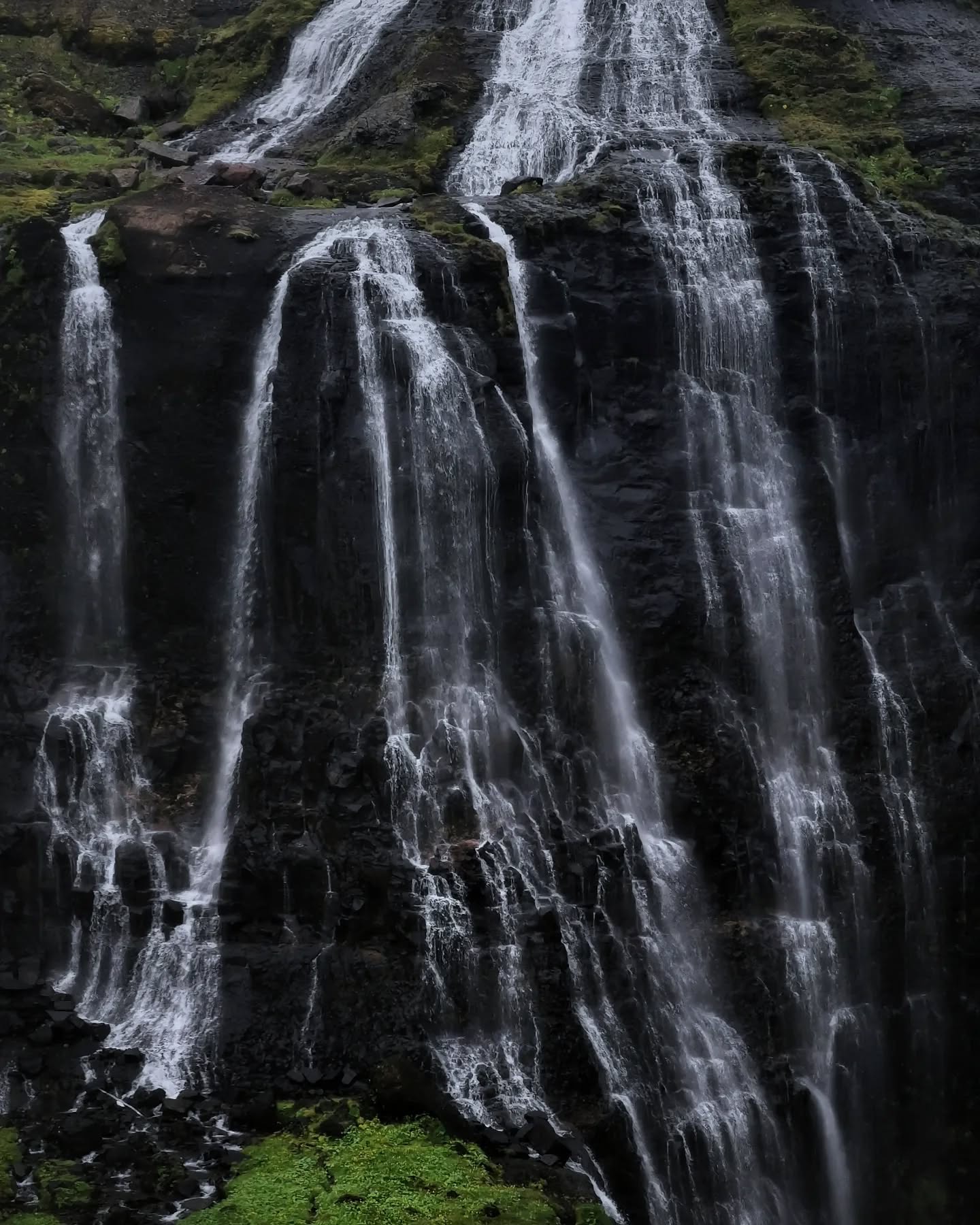 A wide curtain of water falling down a dark rock face