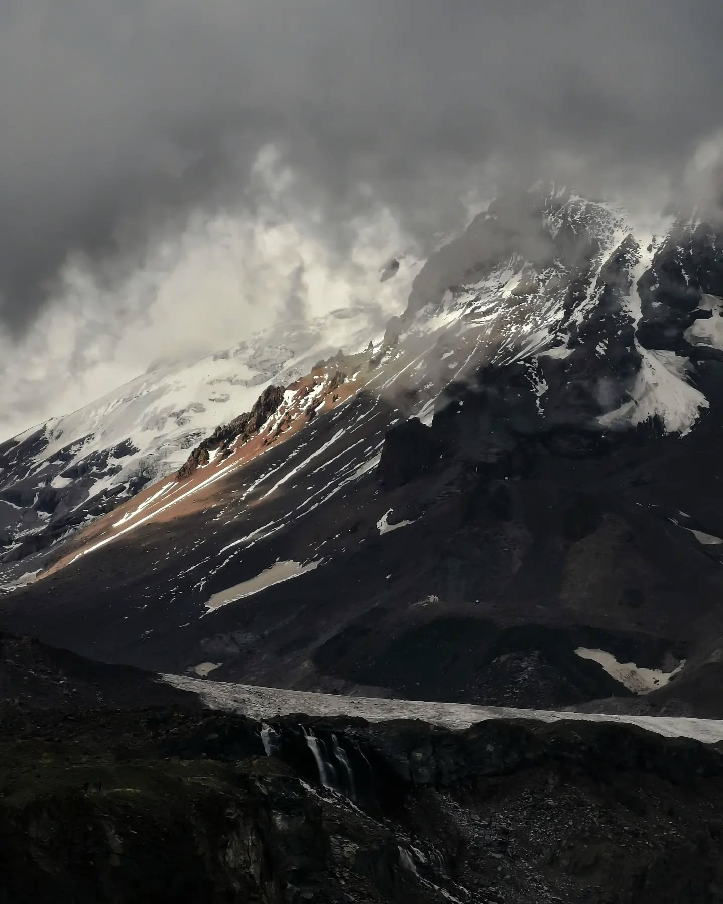 Cloud tearing across a snow-dusted mountain flank