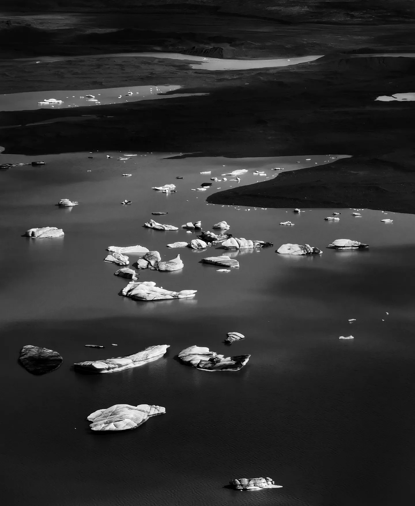 Icebergs drifting on a dark glacial lagoon, in black and white
