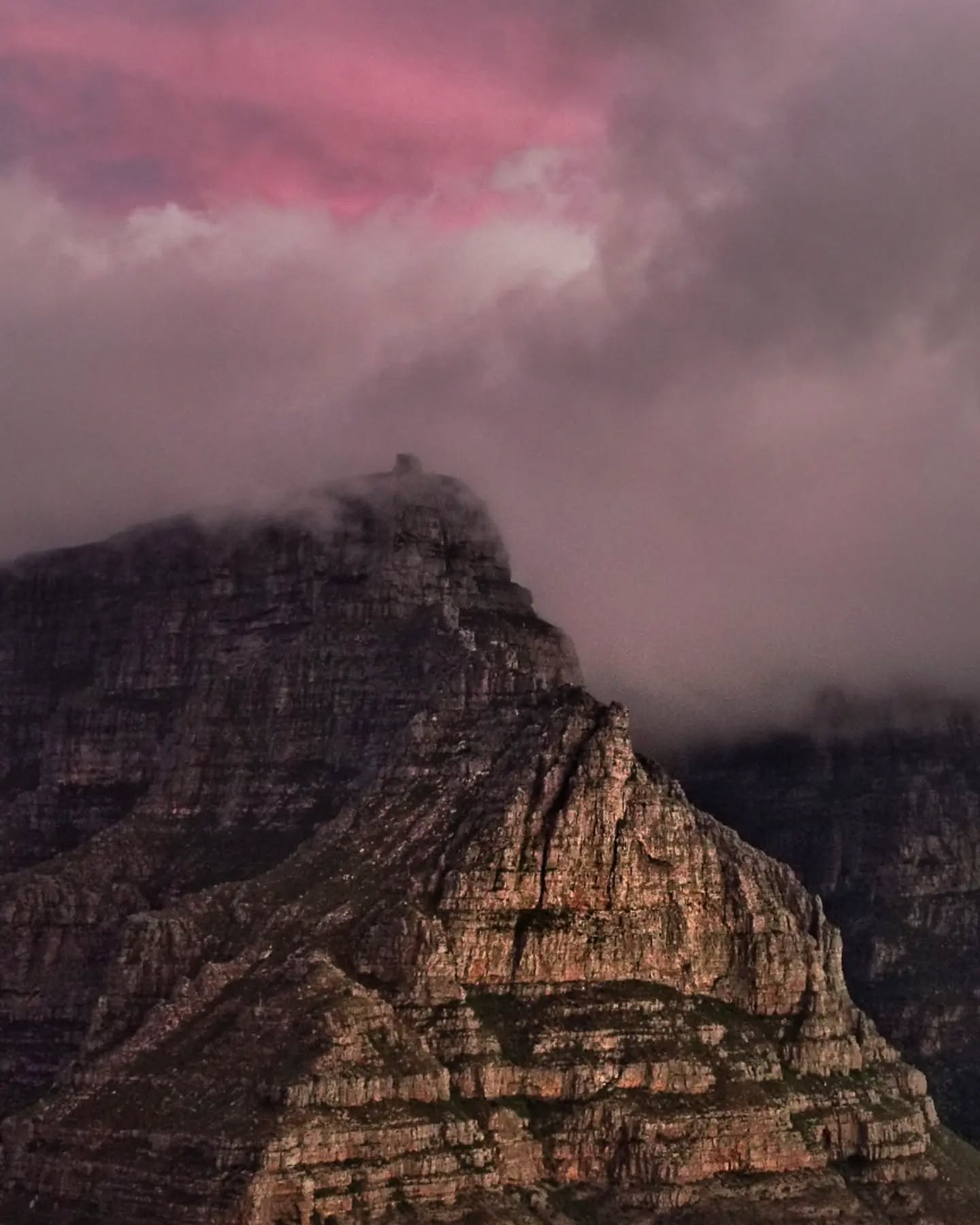 A pink-lit mountain face under heavy cloud