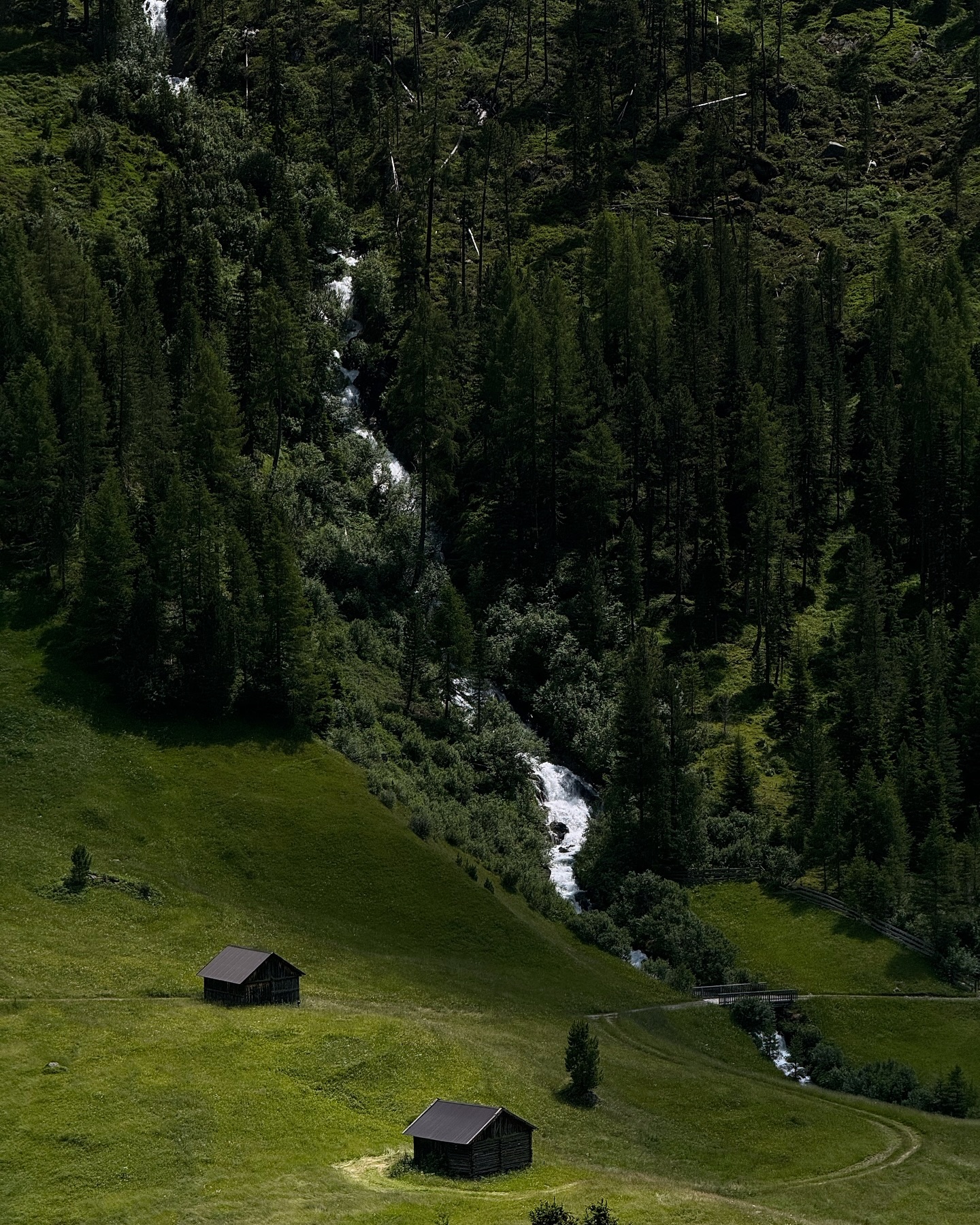 A green alpine valley with a small hut and a thin stream