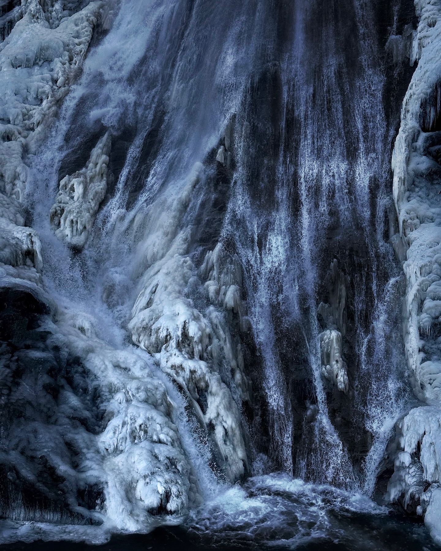 Meltwater cascading down a dark, ice-crusted cliff