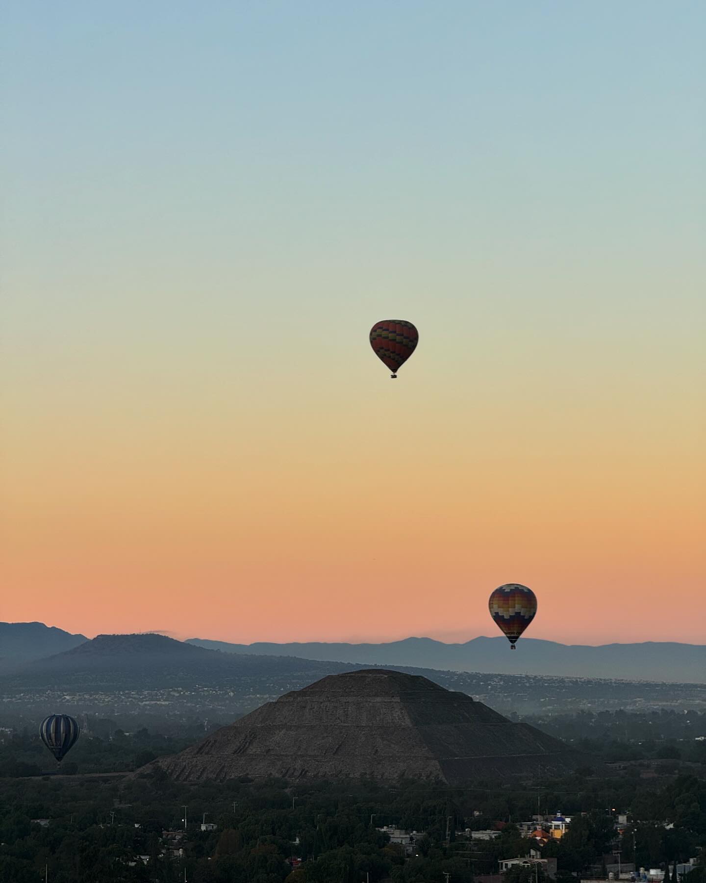 Two hot air balloons drifting over a plain at sunrise