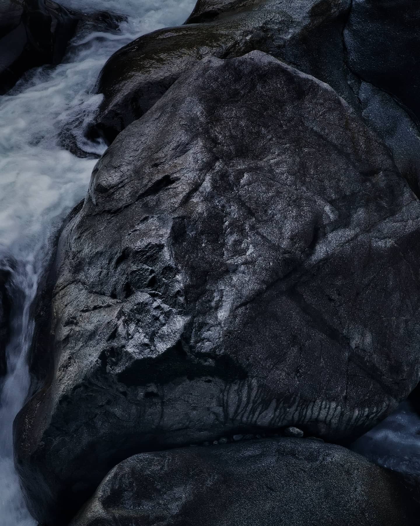 A smooth dark boulder split by rushing water