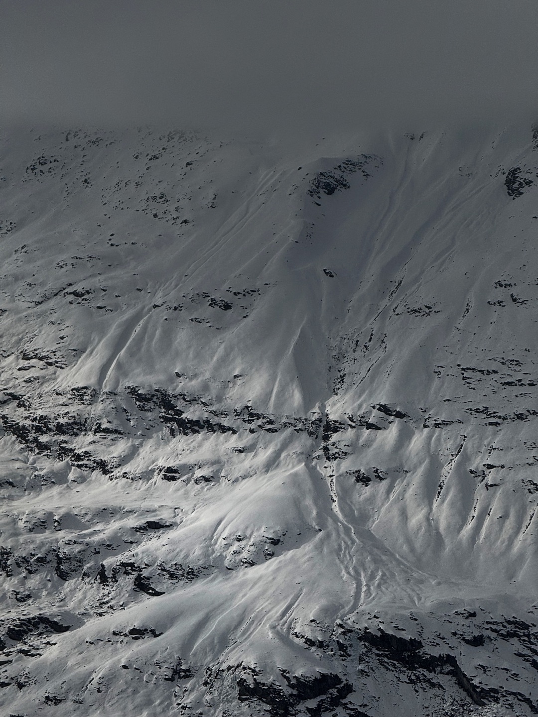 Wind-carved snow and dark rock across a steep mountain face