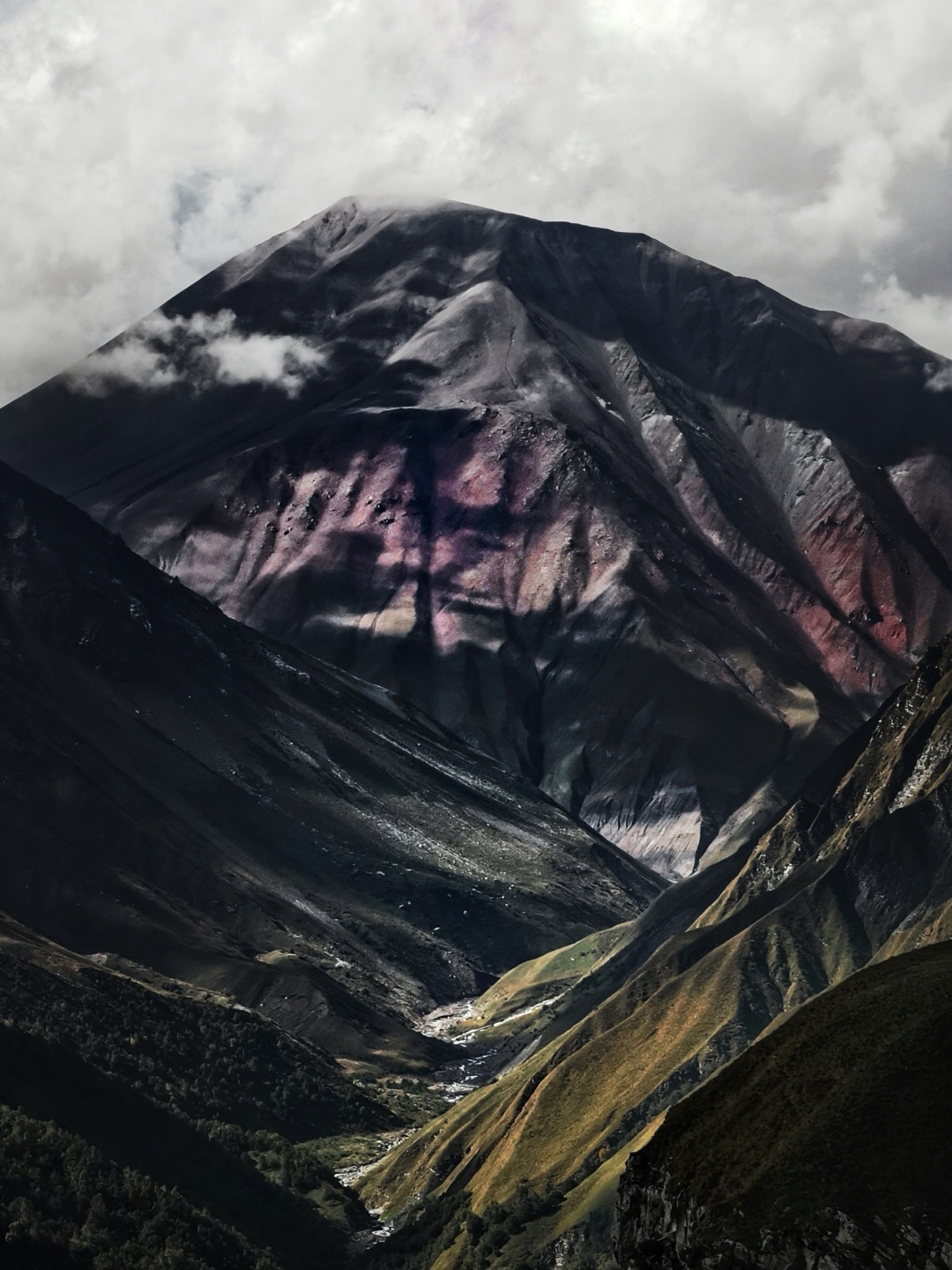 A dark peak streaked with pink and rust-coloured rock above a narrow green valley