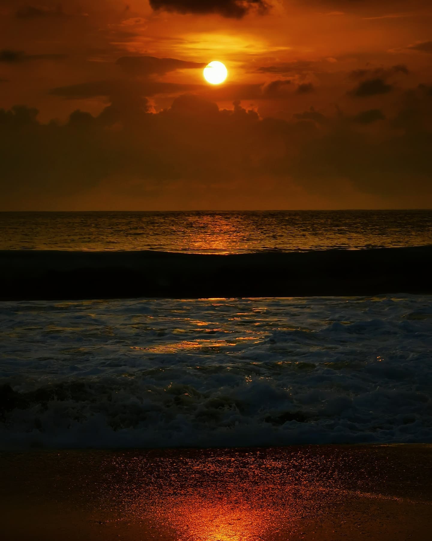 The sun low over the sea, its reflection running up the wet sand through breaking surf
