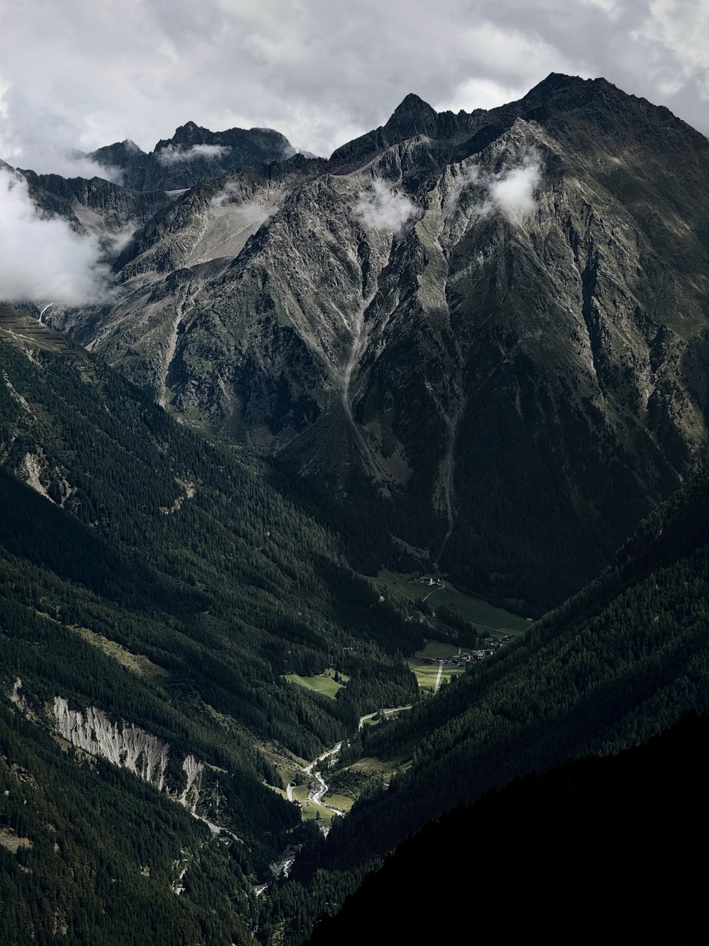 A village on the floor of a deep forested valley under cloud-topped peaks
